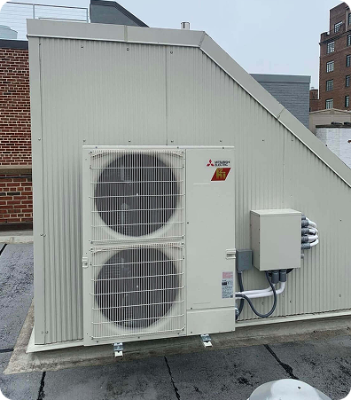 Mitsubishi Electric outdoor HVAC unit with two fans mounted on a beige, corrugated metal enclosure on a flat rooftop against a brick building